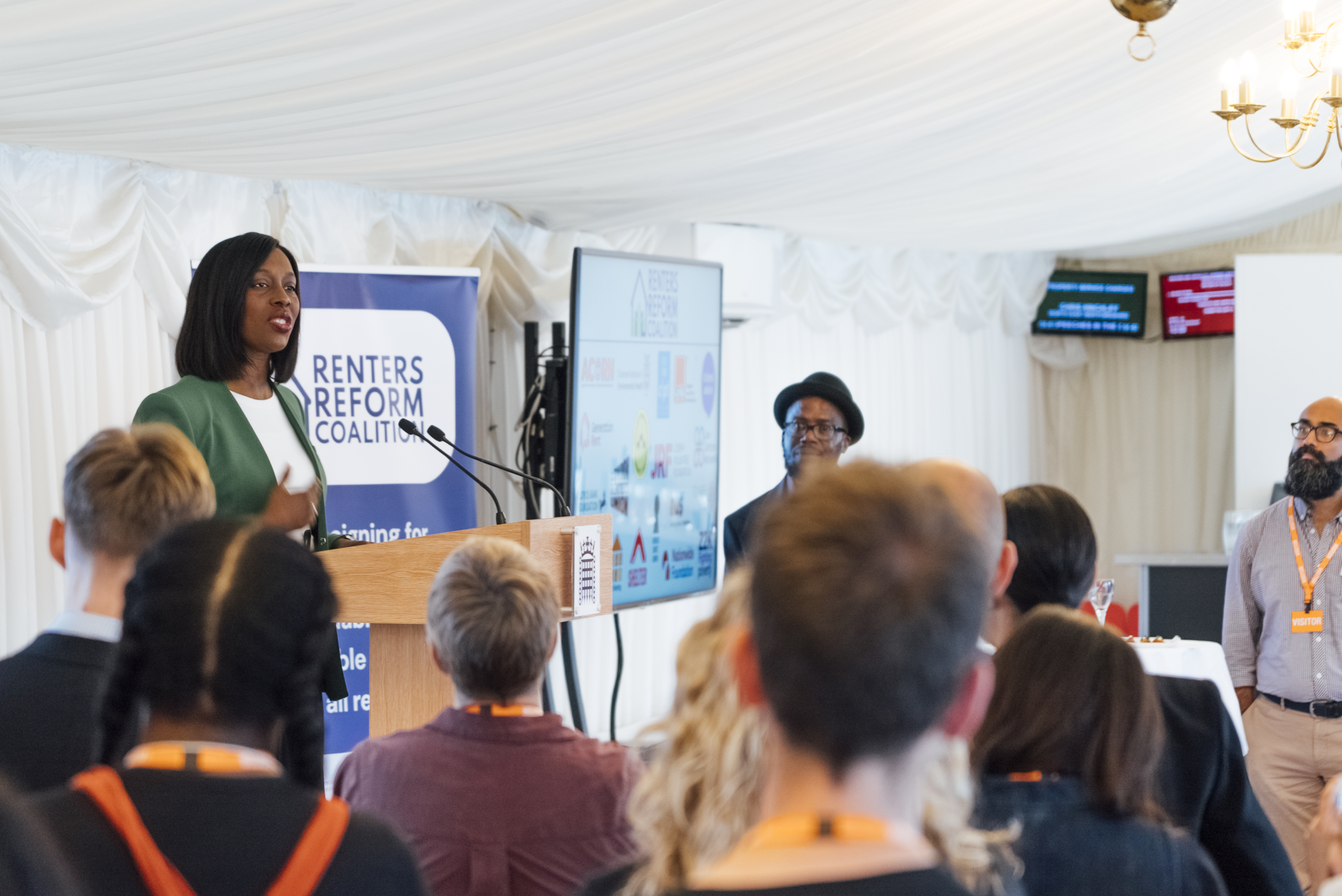 Florence Eshalomi speaks at a podium with people watching, their backs to the camera