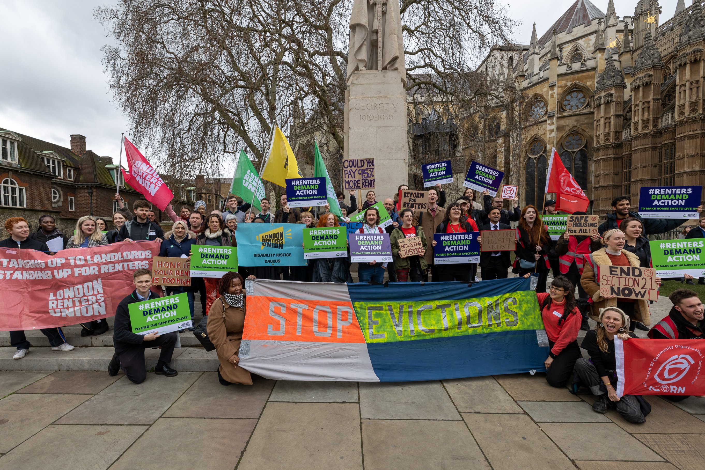 A large group of people holding flags and placards related to ending unfair evictions etc